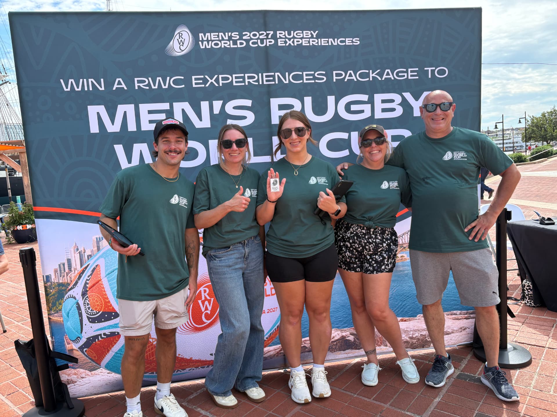 World Rugby event team in front of the Rugby World Cup Experiences backdrop at Baltimore's Inner Harbor
